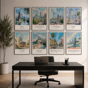 Op de afbeelding: Een verzameling van acht ingelijste kunstprints met stadsgezichten van over de hele wereld: Bali, Montreal, Ontario, Pisa, Rome, Sydney, Beverly Hills en Miami Beach. De prints hangen boven een zwart bureau met een laptop en kantoorbenodigdheden.
