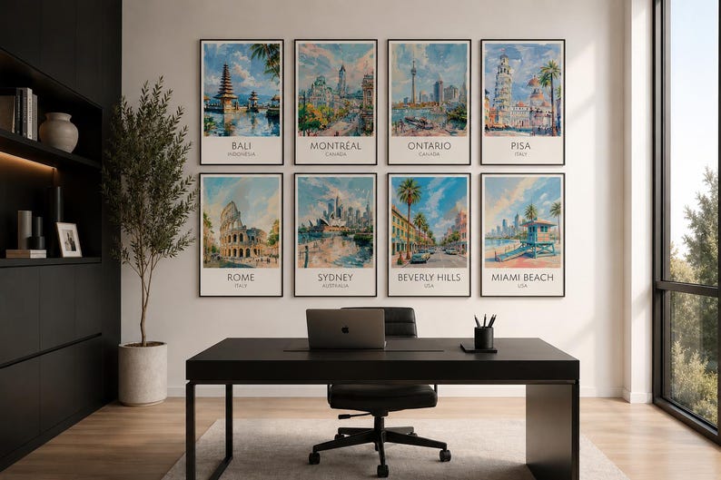 Op de afbeelding: Een verzameling van acht ingelijste kunstprints met stadsgezichten van over de hele wereld: Bali, Montreal, Ontario, Pisa, Rome, Sydney, Beverly Hills en Miami Beach. De prints hangen boven een zwart bureau met een laptop en kantoorbenodigdheden.