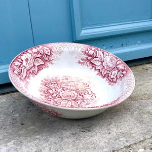 Könnte beinhalten: Eine weiße und rot gemusterte Keramikschale mit Blumenmuster. Die Schale hat ein detailliertes Design aus Blumen und Blättern in einem tiefroten Farbton auf weißem Hintergrund. Der Rand hat eine dekorative Bordüre. Die Schale ist wahrscheinlich Vintage oder antik.