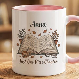 Puede incluir: Una taza de cerámica blanca con interior y asa de color rosa claro. El frente presenta una ilustración de un libro abierto, una taza pequeña y gafas, con el nombre Anna y el texto Just One More Chapter impreso en una fuente cursiva oscura.