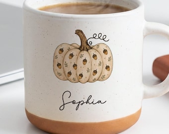 May include: A speckled white ceramic mug with a terracotta-colored base, featuring a central illustration of a pumpkin decorated with small acorn patterns and the name Sophia written in black cursive script below the pumpkin graphic.