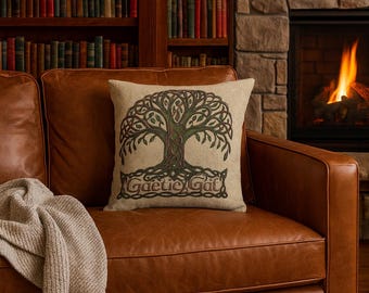 May include: A square beige throw pillow with a Celtic tree of life design in shades of green and brown. The pillow is on a brown leather couch with a beige throw blanket. The text "Gaelic Gat" is at the bottom of the design.