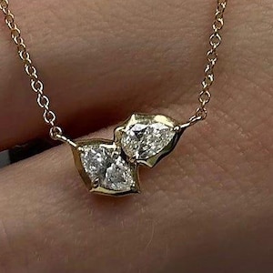 May include: A delicate gold necklace featuring two diamond pendants. The diamonds are set in a gold setting and are of varying shapes. The necklace chain is also gold and is visible against a striped background.