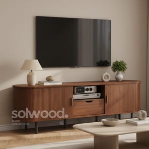 May include: A mid-century modern style wooden TV stand with a ribbed front design. The stand has a drawer, a shelf for electronics, and a cabinet. A lamp, decorative items, and a TV are above the stand. The brand name "solwood." is visible.