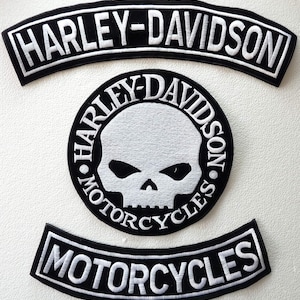 Puede incluir: Tres parches Harley-Davidson en blanco y negro. El parche superior es arqueado y dice "HARLEY-DAVIDSON". El parche central es circular con un diseño de calavera y las palabras "HARLEY-DAVIDSON MOTORCYCLES". El parche inferior dice "MOTORCYCLES".