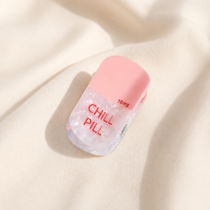 May include: A pill-shaped hair clip featuring a solid light pink top section and a translucent, pearlescent white bottom section. The text CHILL PILL is printed in red on the bottom, with the text 16mg printed in smaller red font above it.