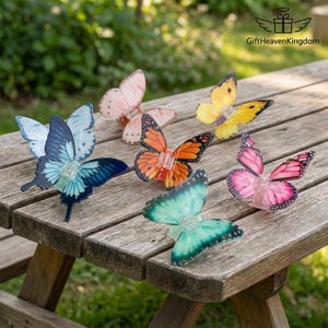 Puede incluir: Una colección de decoraciones de mariposas coloridas con varios diseños de alas, incluyendo azul, naranja, rosa y amarillo. Las mariposas están dispuestas sobre una mesa de madera, lo que sugiere una decoración exterior o de jardín. Cada mariposa tiene una pequeña luz.