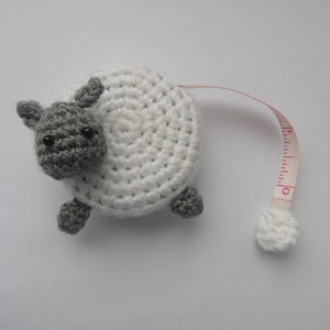May include: A white and grey crocheted sheep-shaped tape measure with a red and white measuring tape.