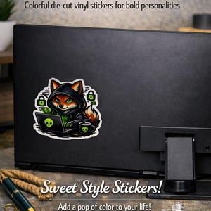 May include: A black laptop with a sticker of a fox in a hoodie, working on a laptop with a skull on the screen. The sticker is surrounded by green padlocks and a skull mug. Text reads "Vibrant Vibes Unleashed."
