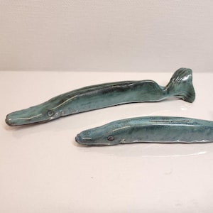 May include: Two ceramic eel-shaped incense holders in shades of teal and blue. The holders have a glossy finish and are designed with a tail and a small opening for incense sticks. The eel-shaped design adds a unique touch to home decor.