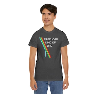 May include: Dark gray t-shirt with the text "FREELOAD KIND OF DAY" in white. The shirt features a colorful design of curved lines in green, blue, and red. The t-shirt is made of a soft material.