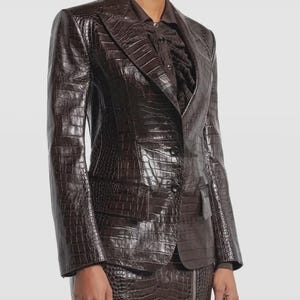 Op de afbeelding: Een bruine, getextureerde blazer en rok set. De blazer heeft een revers, een sluiting met twee knopen en een enkele borstzak. De rok heeft een ritssluiting. De outfit is gemaakt van een materiaal met een krokodillenleerpatroon.