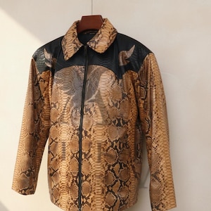 May include: A brown and black snakeskin-patterned jacket with a black collar and yoke. The jacket has a zip closure and long sleeves. The jacket is hanging on a wooden hanger.