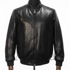 Op de afbeelding: Zwarte leren bomberjack met een slangenhuiddessin. De jas heeft een ritssluiting aan de voorkant, een geribbelde kraag, manchetten en zoom. De jas wordt gepresenteerd op een mannequin met houten armen.