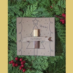 May include: A festive Christmas card with a tree design, featuring the phrases "Ho ho ho!" and "Fijne feestdagen!". The card holds two small items. The image is set against a backdrop of green foliage and red berries.