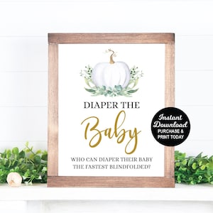May include: A printable sign for a baby shower game, with a white pumpkin and green leaves, reads "Diaper the Baby" and "Who can diaper their baby the fastest blindfolded?"