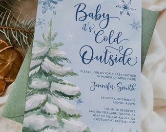 Op de afbeelding: Een uitnodiging voor een babyshower met een winterthema. De uitnodiging toont een aquarel illustratie van een besneeuwde dennenboom en de tekst "Baby it's Cold Outside". Een brandende kaars, gedroogde sinaasappelschijfjes en dennentakken maken de scène compleet.