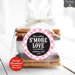 May include: A pink and black round sticker with the text "We're adding S'MORE LOVE to our family Jennifer & Jason 7.12.22". The sticker is on a clear plastic bag filled with graham crackers, chocolate, and marshmallows.