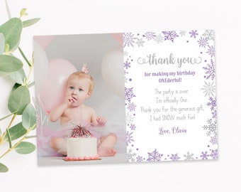 May include: A thank you card with a photo of a baby girl and a birthday cake. The card has a snowflake border and text that reads "thank you for making my birthday ONEderful!" and "Love, Olivia."
