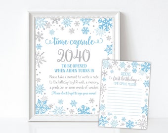 May include: A printable time capsule sign with a snowflake design. The sign says "Time Capsule 2040" and "To be opened when Aiden turns 18". There is a smaller card with a snowflake design that says "Aiden's First Birthday Time Capsule Message".