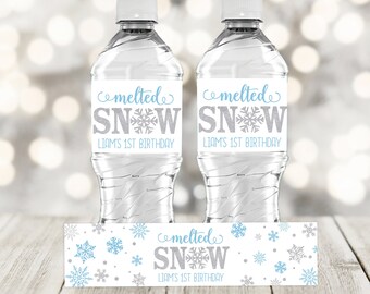 Peut inclure: Deux bouteilles d'eau en plastique transparent avec des étiquettes qui disent "neige fondue" et "1er anniversaire de Liam". Une étiquette plus petite avec le même texte est affichée sous les bouteilles.