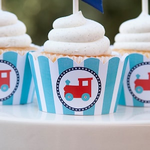 Op de afbeelding: Drie cupcakes met witte frosting en blauwe en witte gestreepte cupcake-vormpjes. Elk cupcake-vormpje heeft een rood treintje-ontwerp.