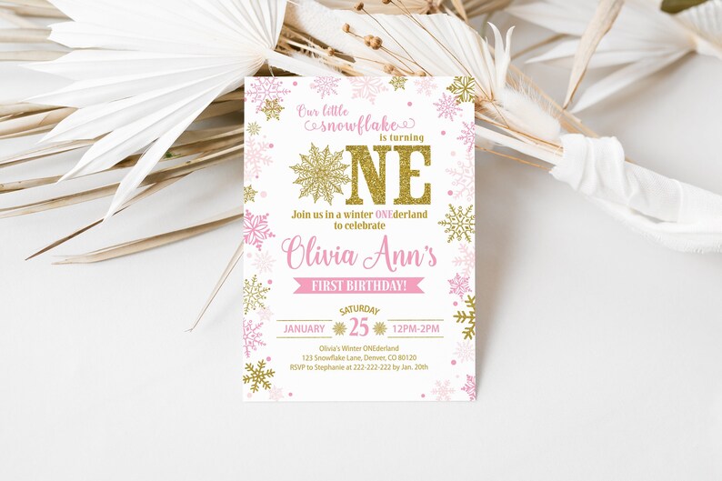 May include: A pink and gold snowflake-themed first birthday invitation for Olivia Ann. The invitation features a large gold glitter "ONE" with snowflakes and pink dots. The text reads "Our little snowflake is turning ONE. Join us in a winter ONEderland to celebrate Olivia Ann's First Birthday! Saturday, January 25, 12PM-2PM. Olivia's Winter ONEderland, 125 Snowflake Lane, Denver, CO 80120. RSVP to Stephanie at 222-222-222 by Jan. 20th."