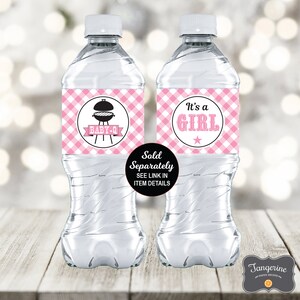 May include: Two clear plastic water bottles with pink and white gingham patterned labels. The labels have black text that reads "It's a Girl" and "Baby Q" with a grill graphic. The labels also have a white star and a white circle around the text.