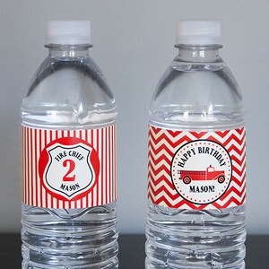 以下が含まれることがあります： 赤と白のラベルが付いた透明なプラスチック製の水筒が2本。1つのラベルには赤い消防車と「ハッピーバースデーメーソン！」という文字が書かれています。もう1つのラベルには赤と白のストライプの背景に「消防署長2メーソン」と書かれた盾があります。