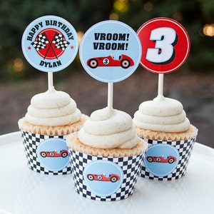 May include: Three cupcakes decorated with racing car themed toppers. The cupcakes have white frosting and are topped with a checkered cupcake liner. The toppers are round and feature a red race car, a checkered flag, and the number 3.