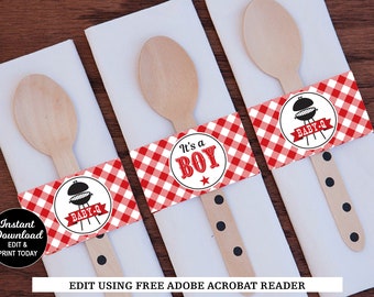 Op de afbeelding: Drie houten lepels met rood-wit geblokte papieren banden. De banden hebben een zwart-witte grillgrafiek en de tekst "BABY-Q". Een band heeft de tekst "Het is een JONGEN" met een rode ster.