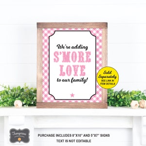 May include: Pink and white gingham print sign with the text "We're adding S'MORE LOVE to our family!" in black text. The sign is framed in wood and has a white star in the bottom center. The sign is 8" x 10" and is sold separately.