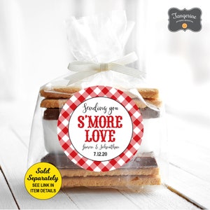 May include: A red and white gingham patterned circle sticker with the text "Sending you S'MORE LOVE Lauren & Johnathan 7.12.20" on a clear plastic bag filled with graham crackers, chocolate, and marshmallows.