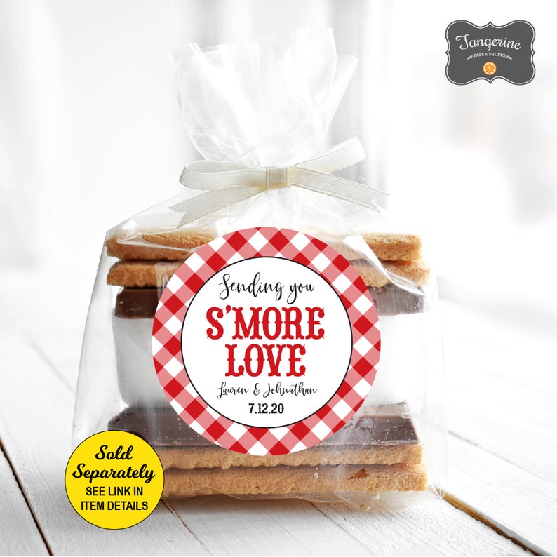 May include: A red and white gingham patterned circle sticker with the text "Sending you S'MORE LOVE Lauren & Johnathan 7.12.20" on a clear plastic bag filled with graham crackers, chocolate, and marshmallows.