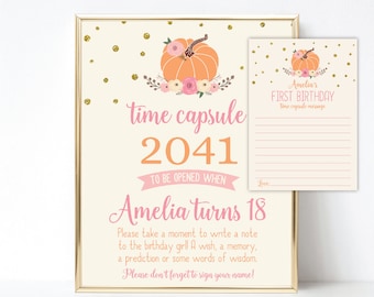 Może przedstawiać: Oprawiony znak kapsuły czasu i pasująca karta. Znak zawiera ilustrację dyni, tekst "time capsule 2041" i instrukcje na 18. urodziny Amelii. Na karcie widnieje napis "Amelia's FIRST BIRTHDAY" i miejsce na wiadomość.