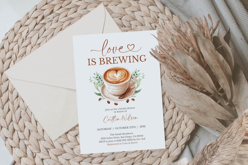 K&ouml;nnte beinhalten: Eine Einladung zur Brautparty mit dem Text "love is brewing" und einem Aquarellbild einer Kaffeetasse mit einem herzf&ouml;rmigen Design im Schaum. Die Einladung befindet sich auf wei&szlig;em Hintergrund mit einem Umschlag und Trockenblumen.