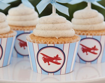 May include: Close-up of cupcakes decorated with white frosting and topped with blue and white striped paper liners featuring red airplane silhouettes.