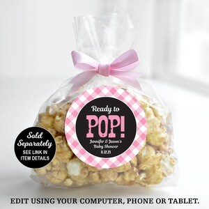 May include: A clear plastic bag filled with popcorn, tied with a pink ribbon. A round sticker with a pink and white gingham pattern and black text reads "Ready to POP! Jennifer & Jason's Baby Shower 8.12.21". A smaller black circle sticker reads "Sold Separately SEE LINK IN ITEM DETAILS".
