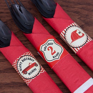 Puede incluir: Anillos de servilleta a rayas rojas y blancas con un camión de bomberos, una insignia de jefe de bomberos y un diseño de sombrero de bombero. Los anillos dicen "¡Feliz cumpleaños Mason!" y "Jefe de bomberos 2 Mason".