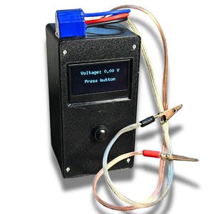 May include: A black electronic device with a small screen displaying "Voltage: 0.00 V" and "Press button." It has a blue connector, a black button, and wires with alligator clips. The device appears to be a voltage tester.