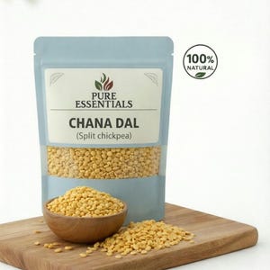 Puede incluir: Un paquete azul claro de Chana Dal (garbanzos partidos) con una etiqueta "Pure Essentials" y un sello "100% Natural". El paquete contiene garbanzos partidos amarillos. Un pequeño cuenco de madera y una tabla de cortar de madera también están en la imagen.