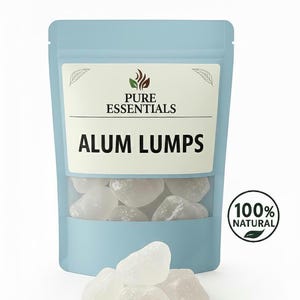 May include: A light blue pouch labeled "PURE ESSENTIALS" with the text "ALUM LUMPS." The pouch has a clear window showing white, irregularly shaped alum lumps. A "100% NATURAL" seal is on the right. Some lumps are outside the pouch.