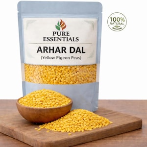 Puede incluir: Un paquete de Arhar Dal (Guisantes Amarillos) de Pure Essentials, con un cuenco de madera y un montón de lentejas amarillas sobre una tabla de cortar de madera. El paquete tiene una ventana transparente.