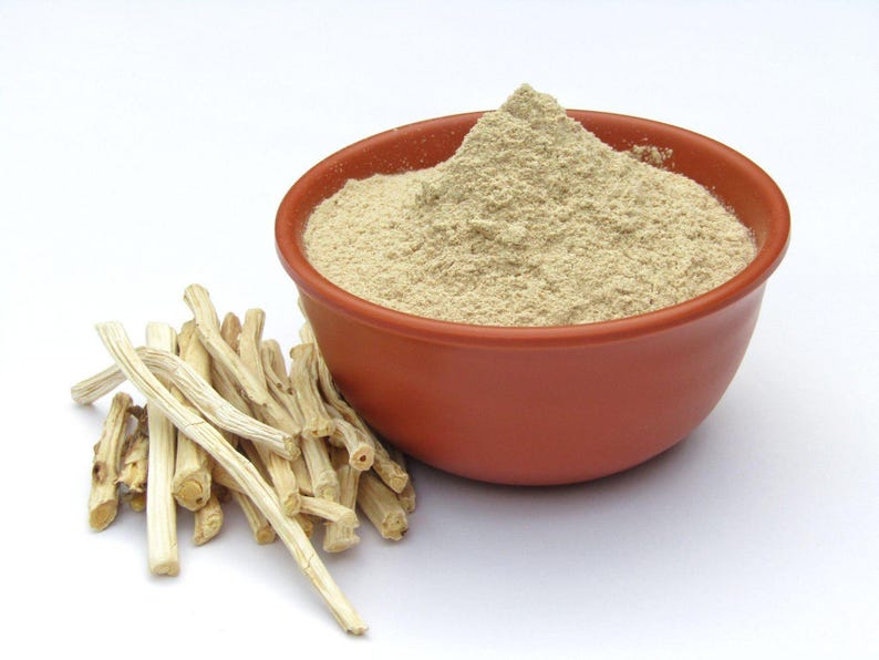 Puede incluir: Un cuenco de terracota lleno de polvo marr&oacute;n claro, probablemente una especia o suplemento, se encuentra junto a un mont&oacute;n de tallos de plantas beige y secos. Los elementos est&aacute;n sobre un fondo blanco.