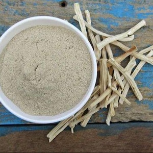 Puede incluir: Un cuenco blanco lleno de polvo marr&oacute;n claro se encuentra junto a un mont&oacute;n de palitos secos de color claro. Los elementos est&aacute;n sobre una superficie de madera desgastada con pintura azul y marr&oacute;n.