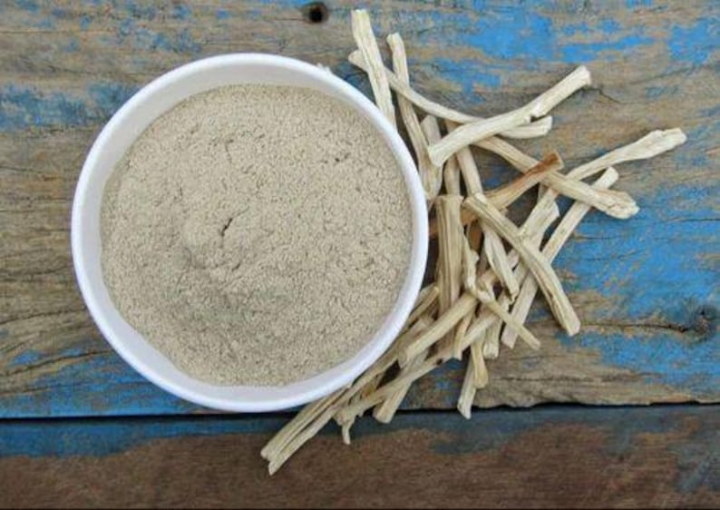 Puede incluir: Un cuenco blanco lleno de polvo marr&oacute;n claro se encuentra junto a un mont&oacute;n de palitos secos de color claro. Los elementos est&aacute;n sobre una superficie de madera desgastada con pintura azul y marr&oacute;n.