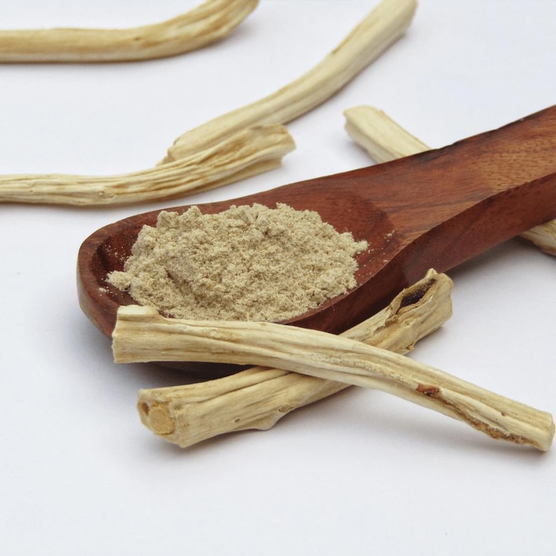 Puede incluir: Una cuchara de madera llena de un polvo marr&oacute;n claro se encuentra entre varios trozos de ra&iacute;ces secas de color beige. Las ra&iacute;ces son largas y cil&iacute;ndricas, con una superficie texturizada. El fondo es blanco.