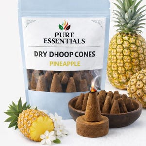 Puede incluir: Un paquete de conos de dhoop secos "Pure Essentials" con aroma a piña. La imagen muestra un cono encendido, un cuenco de madera con conos y piñas frescas. Los conos son marrones y las piñas son amarillas y verdes.