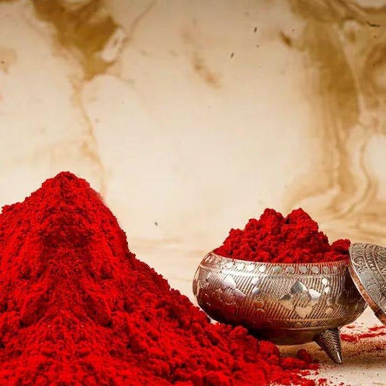 May include: A vibrant image showcases a pile of bright red powder next to a decorative silver bowl filled with the same powder. The bowl has a lid and is resting on three small feet. The background has a marbled effect.