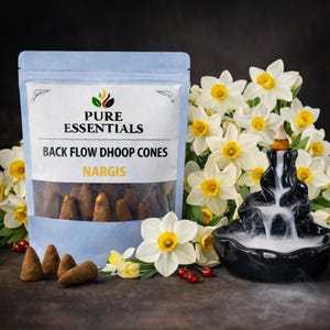 Könnte beinhalten: Eine transparente Plastiktüte mit braunen Backflow-Dhoop-Kegeln mit der Aufschrift "Nargis" steht neben einem schwarzen Keramik-Wasserfall-Räuchergefäß mit weißem Rauch. Weiße Narzissen mit gelben Zentren umgeben die Produkte.